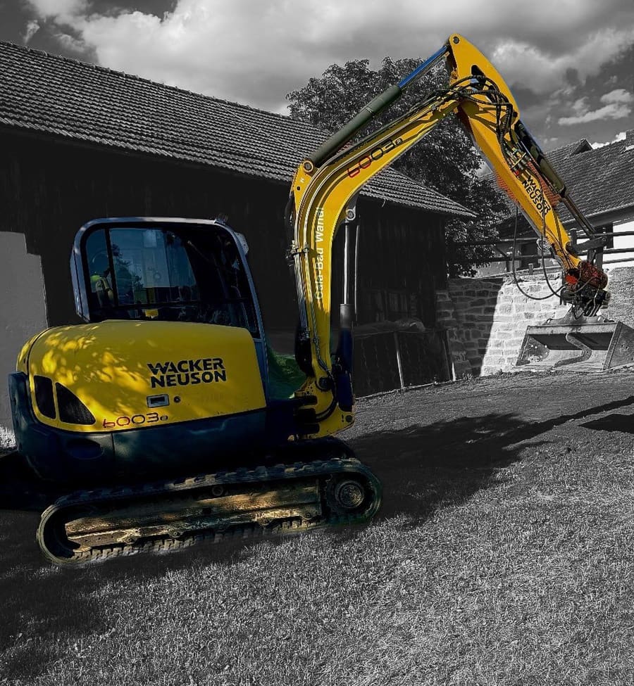 Unser gelber Bagger bei Erdarbeiten vor einer Mauer aus Natursteinen