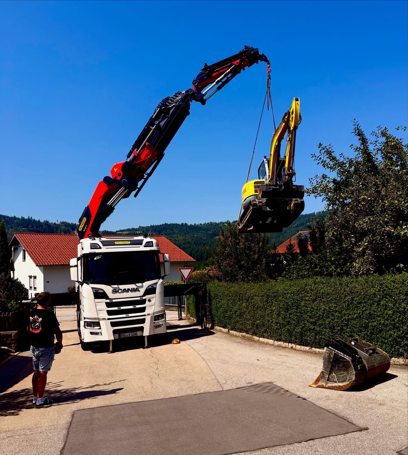 Ein Autokran hebt unseren Bagger über eine Hecke in einen Garten